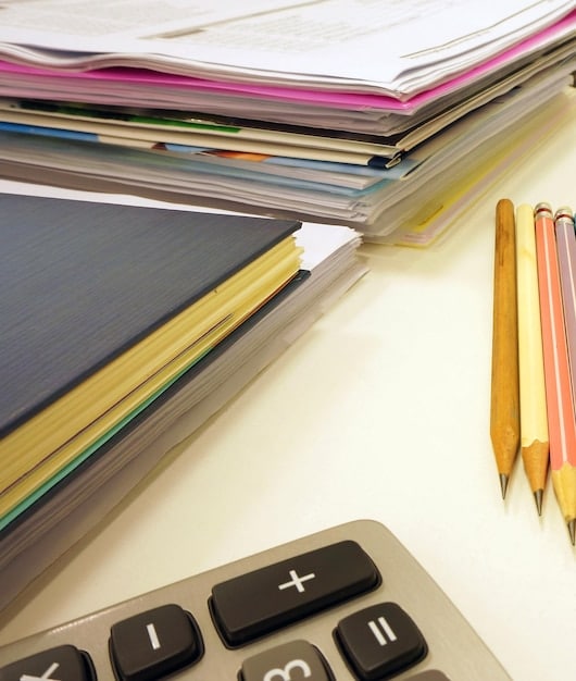 A stack of different colored bank statements on a desk, with a pen and calculator, implying a review of financial documents for tax purposes.